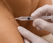 Mãos de luvas fazendo a aplicação com seringa na região marcada.